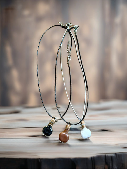 Three necklaces with mini glass cork screw top vials, one each filled with black salt, red brick dust, and camphor.